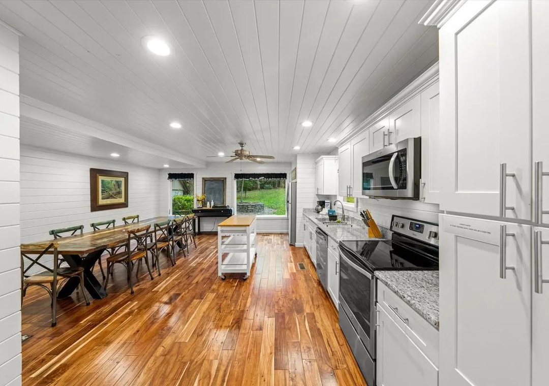 Spacious open-plan kitchen and dining area with gleaming hardwood floors, white shiplap walls, fully equipped kitchen, and large farmhouse table—perfect for gathering and creating memories.