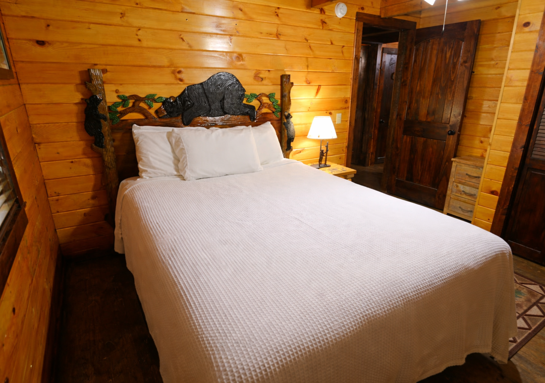Sleep soundly in your cozy cabin bedroom with rustic log walls, handcrafted headboard, and warm bedside lighting creating the perfect mountain retreat atmosphere.