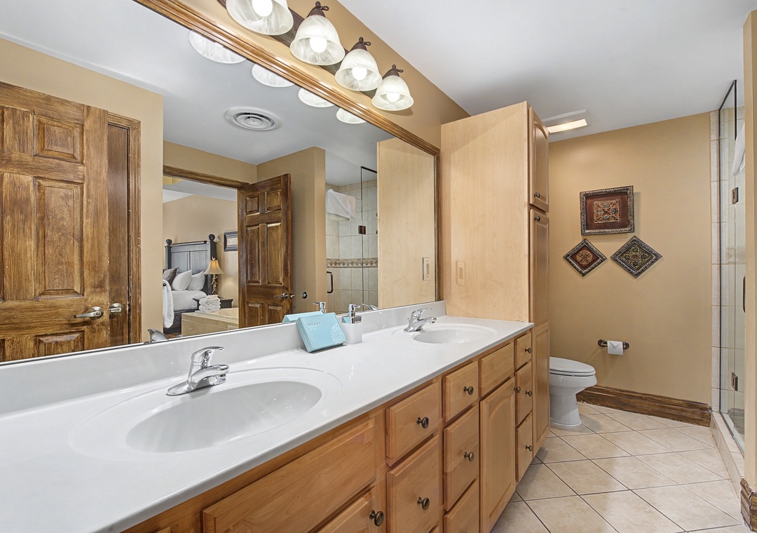 Unwind in your spacious bathroom featuring dual vanities, warm wood cabinetry, and elegant lighting for your morning routine.