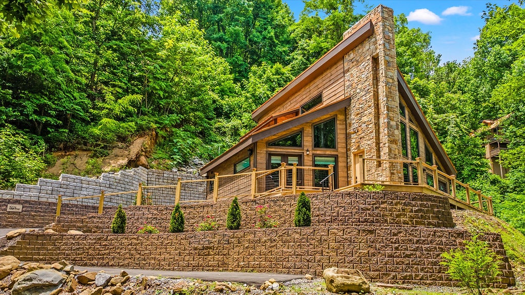 Beautiful A-frame cabin with stone chimney nestled in lush forest surroundings, offering a private woodland retreat.