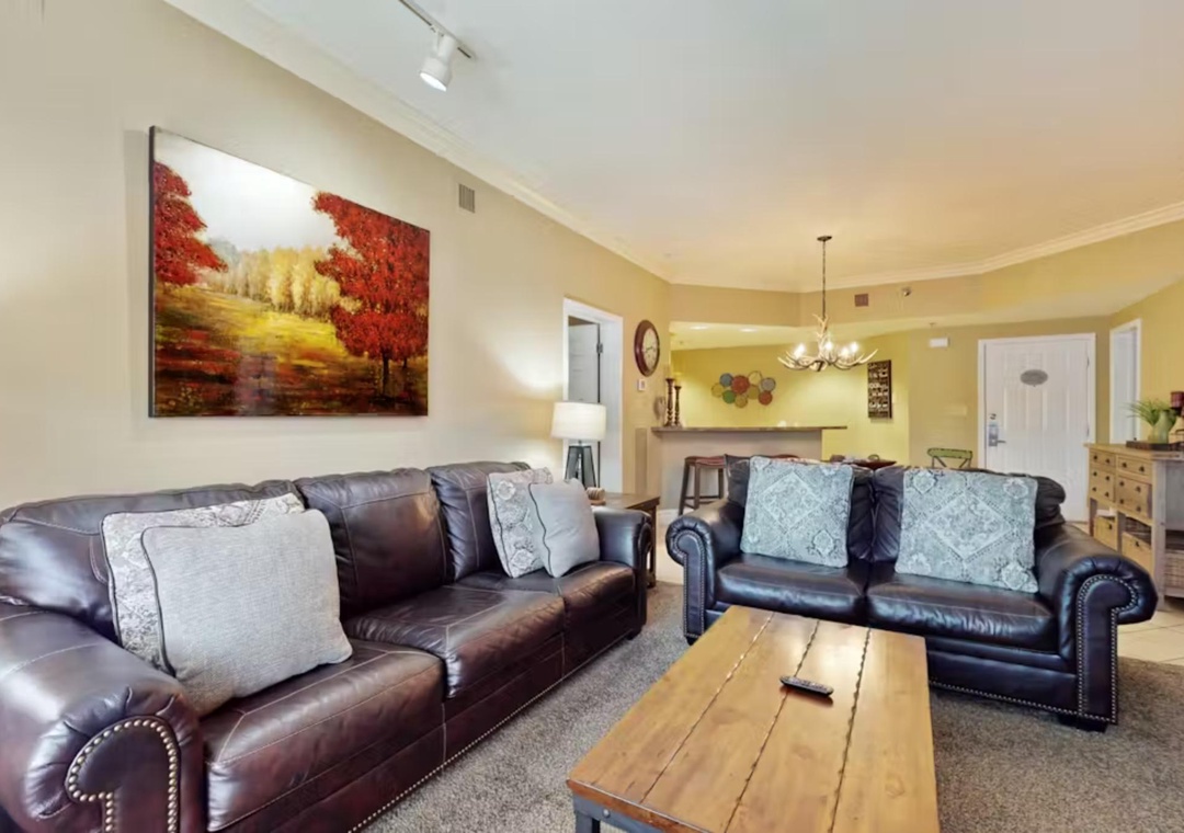 Sink into rich leather sofas in your spacious living room, where autumn artwork and warm lighting create the perfect retreat.