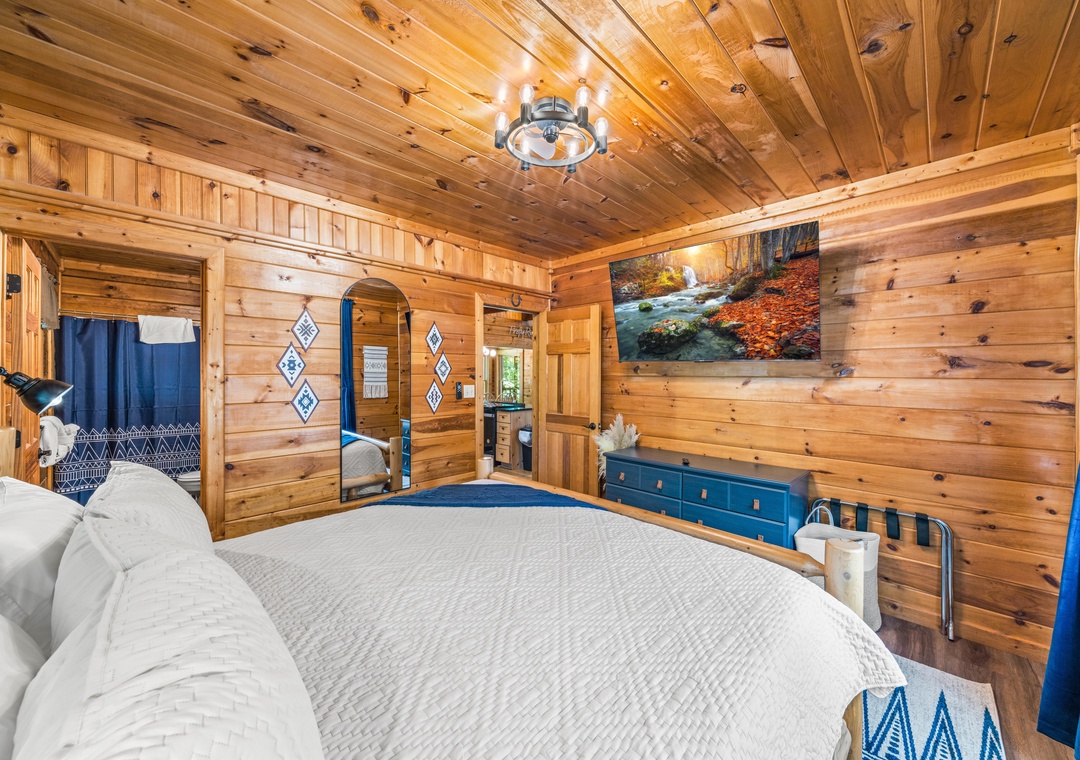 Step into your rustic retreat with warm knotty pine walls, a plush quilted bed, and charming blue accents that invite you to unwind and embrace mountain cabin comfort.