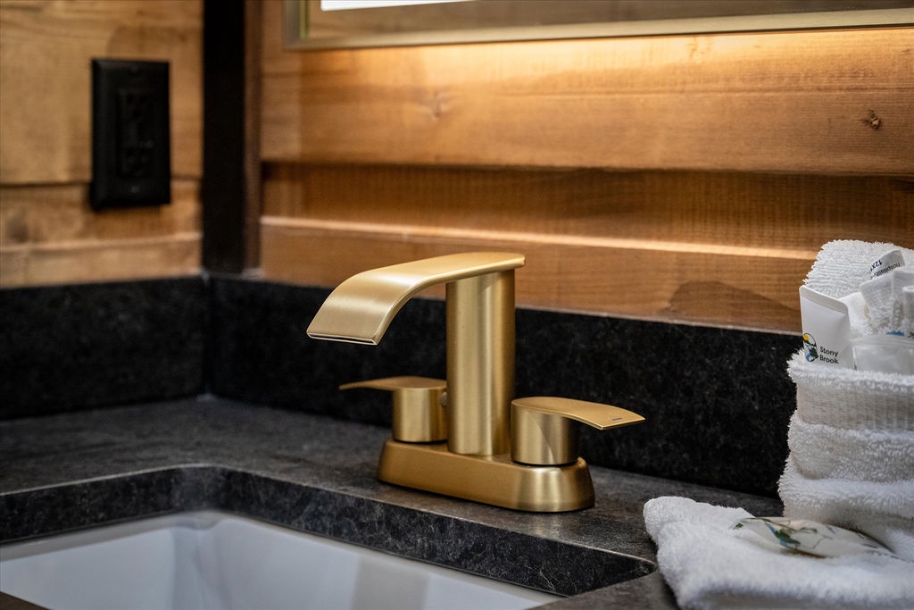 Unwind in your private bathroom featuring elegant brass fixtures, black granite countertops, and plush towels waiting for you. The warm wood accents create a cozy, spa-like retreat.