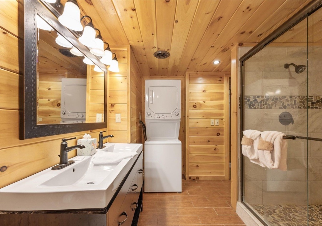 Unwind in your rustic-modern bathroom featuring warm wood walls, sleek vanity, spacious glass shower, and convenient in-unit laundry.