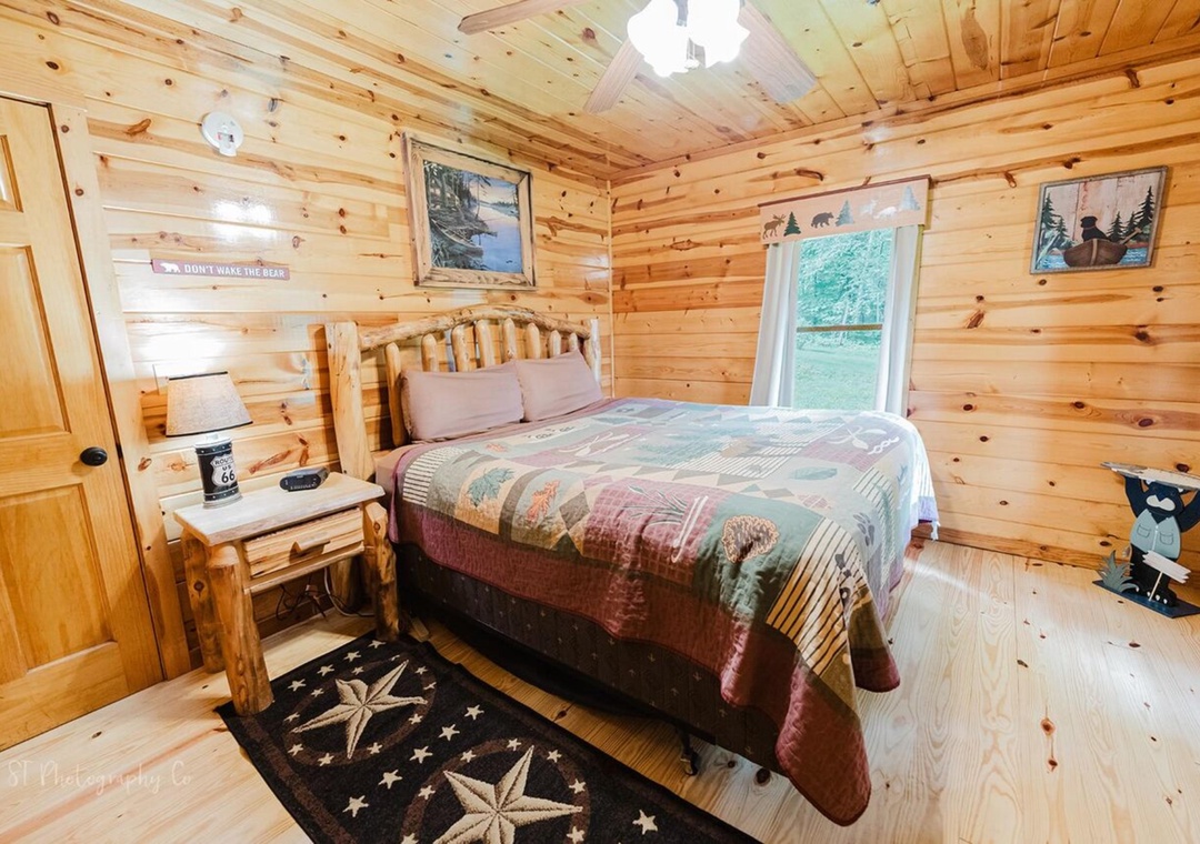 Step into your cozy cabin bedroom where warm pine walls and rustic log furniture create an inviting retreat. Sunlight filters through your window, highlighting woodland artwork and handmade quilts that make this peaceful space truly yours.