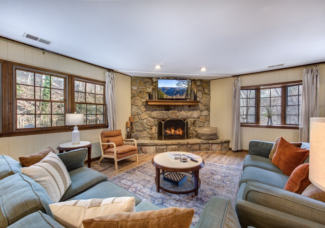 Cozy up by your stone fireplace with mountain views on the TV, surrounded by plush seating perfect for relaxing evenings.