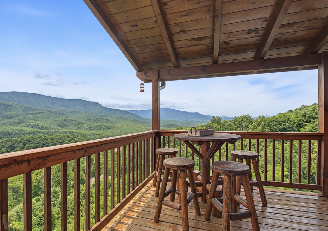 Covered deck with high-top seating offers sweeping mountain and forest panoramas, ideal for morning coffee or evening relaxation in the surrounding natural beauty.
