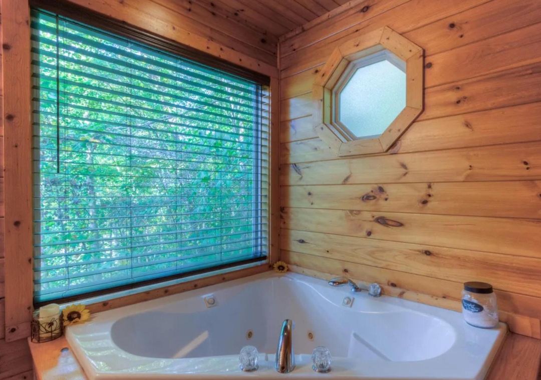 Soak in your private jetted tub surrounded by warm wood walls, with lush forest views filtering through the window—your peaceful retreat awaits.