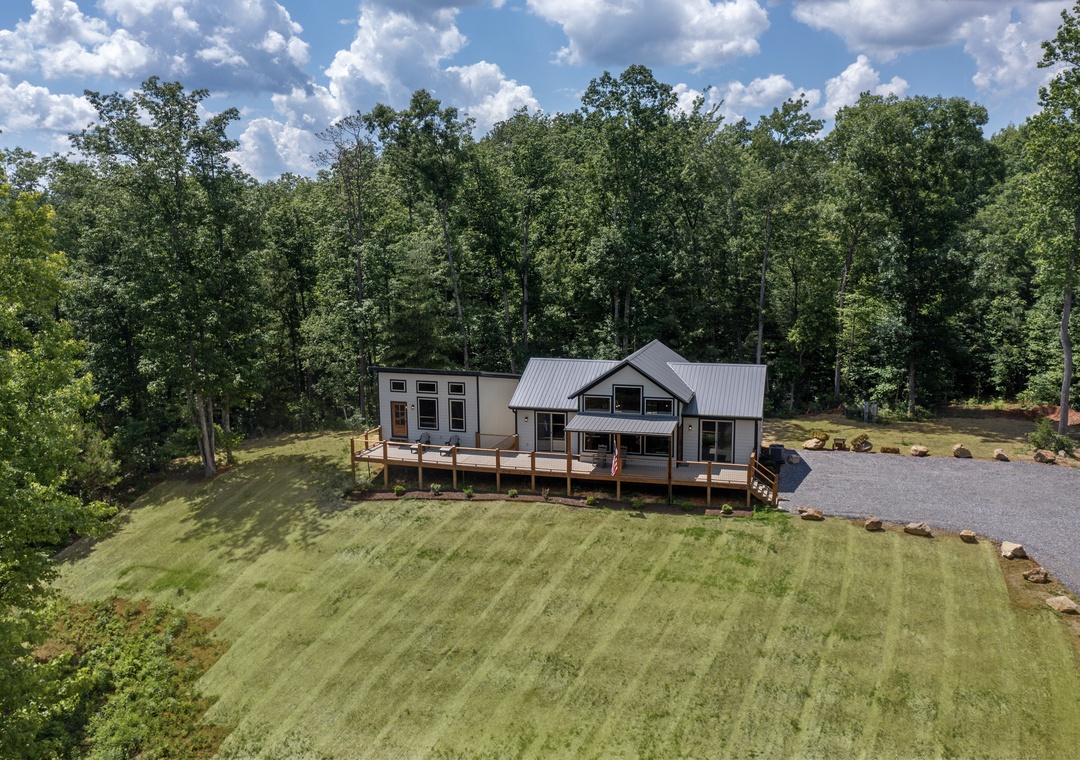 Modern farmhouse-style vacation rental nestled on a private wooded lot with spacious wraparound deck, offering serene natural surroundings and ample outdoor space.