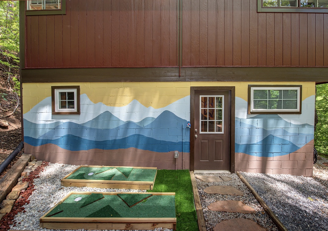 A unique property entrance features an artistic mountain-range mural and a dedicated miniature golf setup on the grounds, surrounded by natural wooded scenery.