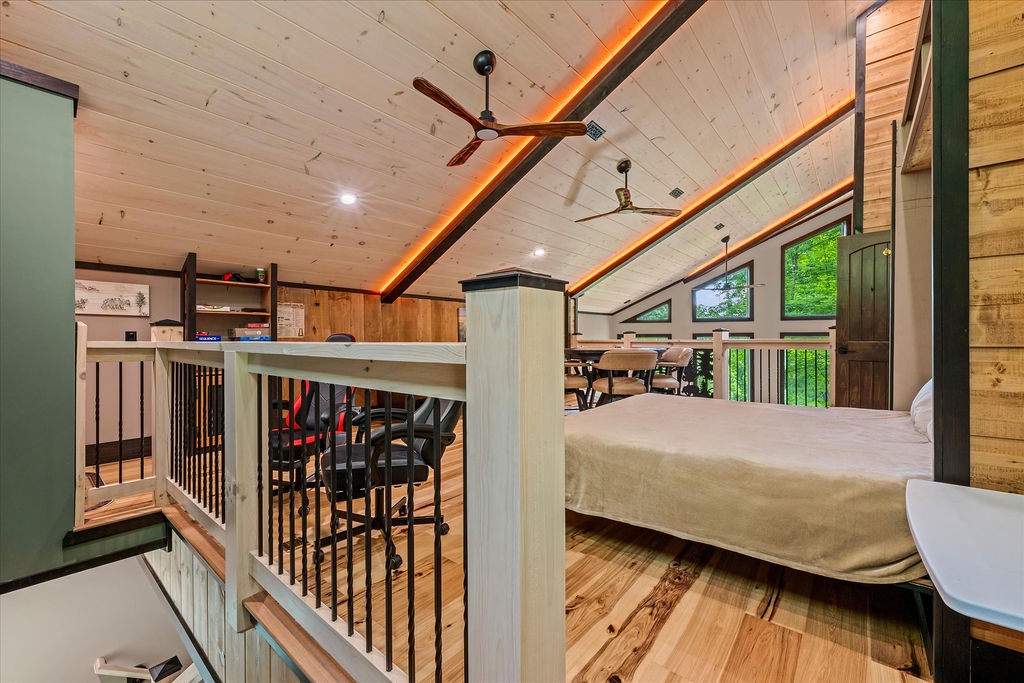 Your cozy loft bedroom features vaulted ceilings with warm wood planks and ambient lighting, creating a restful retreat above the main living space with views of lush greenery.