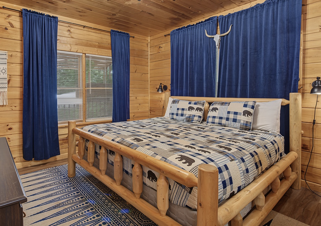 Cozy log cabin bedroom with rustic cedar frame, soft blue plaid linens, and warm wood paneling—your peaceful retreat awaits after days spent exploring.