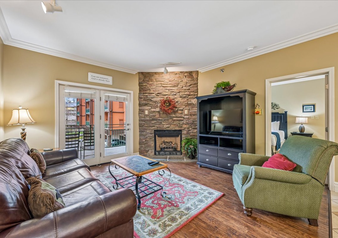 Unwind in your cozy living room with a stone fireplace, plush seating, and peaceful balcony access for relaxing evenings.