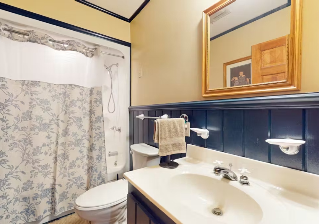 Step into your charming bathroom with classic navy wainscoting, elegant floral wallpaper, and thoughtful touches like fresh towels awaiting your arrival.