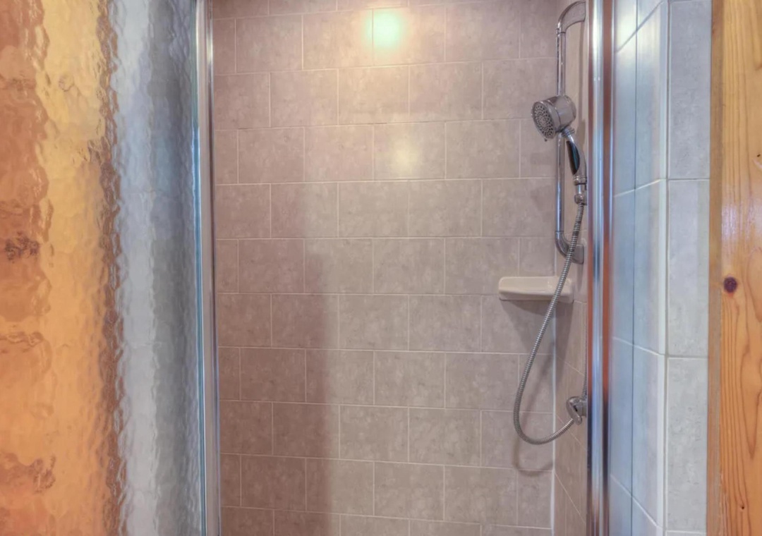 Step into your private shower with modern tilework and a handheld showerhead. The warm wood and stone accents create a spa-like retreat where you can unwind after exploring the area.