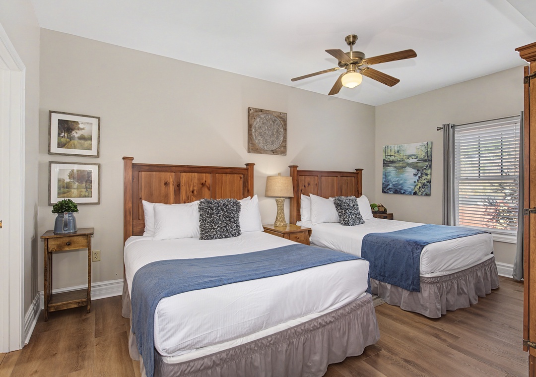 Your spacious bedroom features two comfortable beds with crisp linens, warm wood furnishings, and a ceiling fan for perfect climate control.