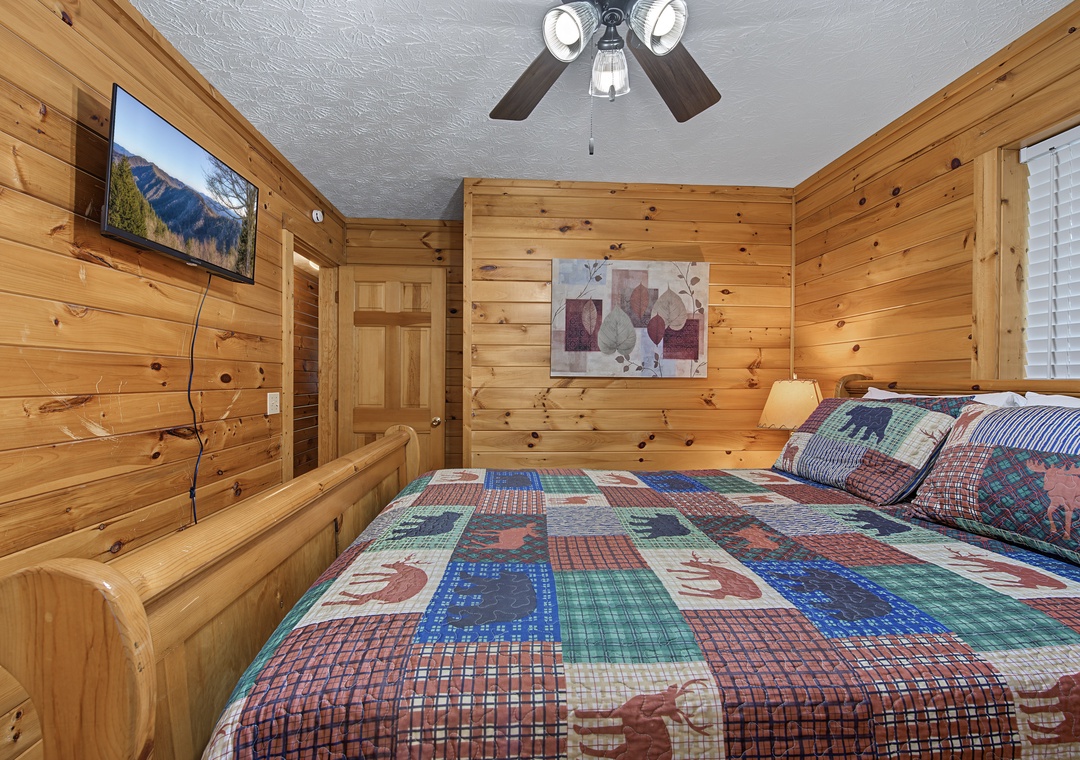 Unwind in your cozy log-cabin bedroom with charming wood walls, a plush quilt, a ceiling fan overhead, and a flat-screen TV for your favorite shows.
