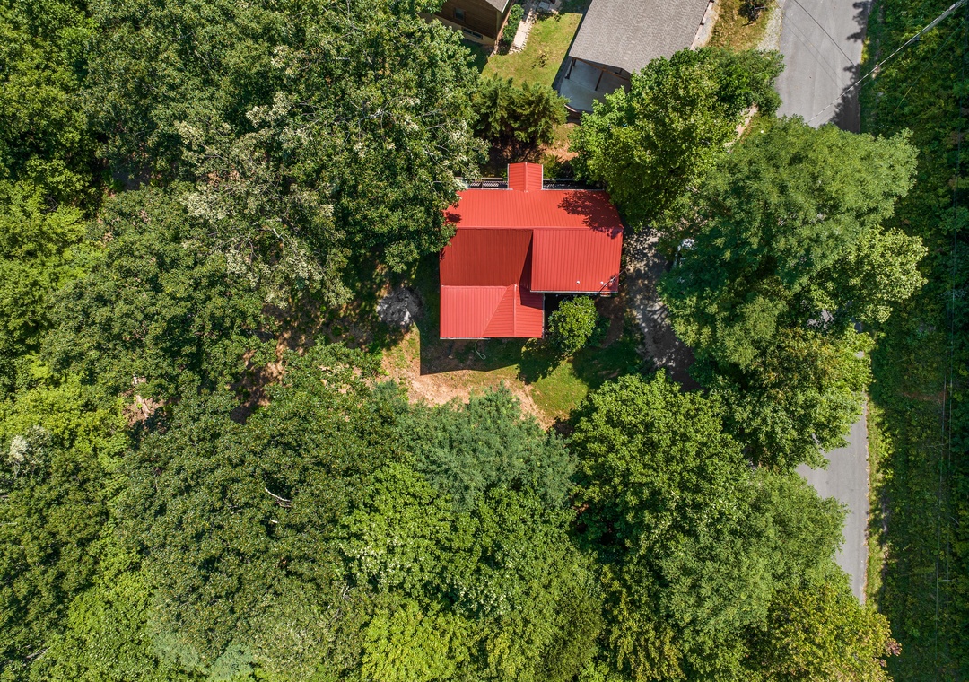 A charming property with a distinctive red roof nestled among lush greenery, offering a peaceful retreat surrounded by towering trees and natural landscape.