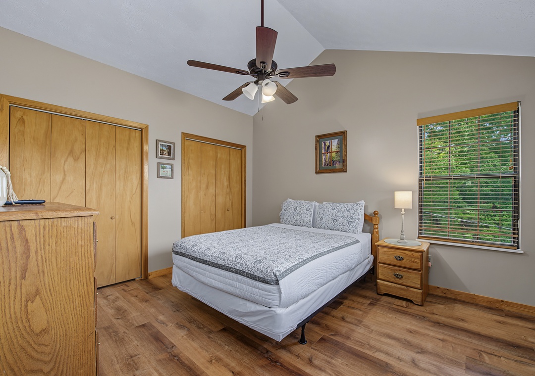 Drift off in your peaceful bedroom, where soft linens and a ceiling fan ensure restful nights, and morning light streams through the window overlooking lush greenery.
