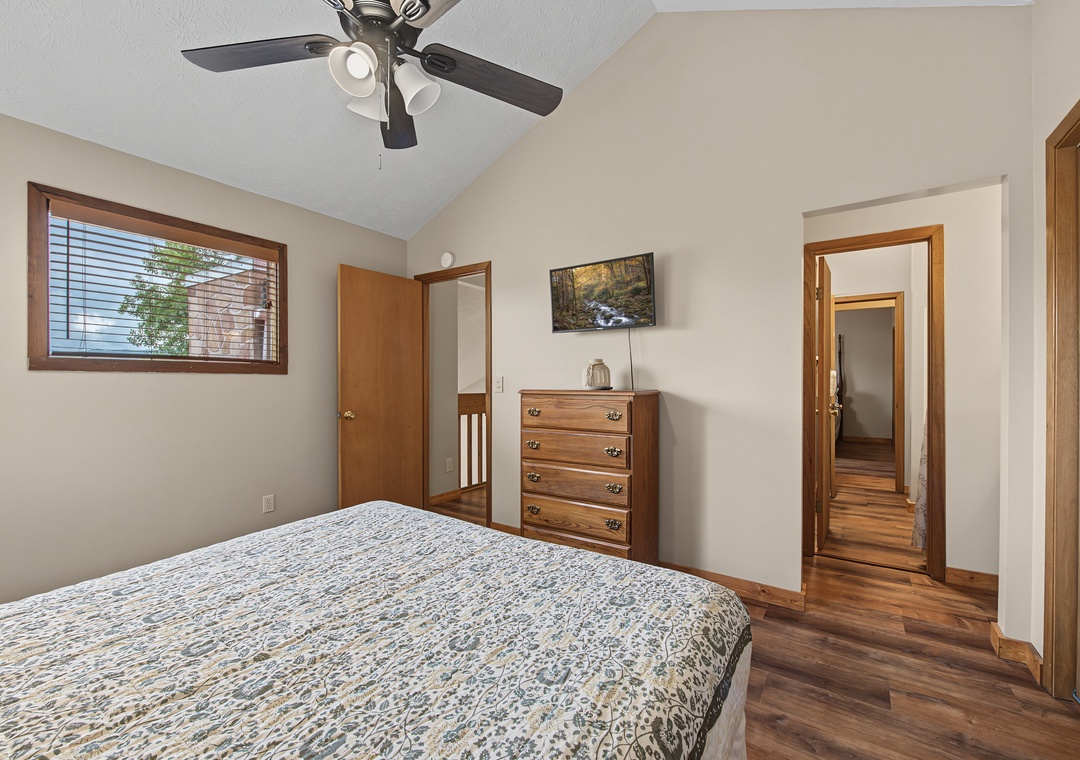 Unwind in your cozy bedroom with warm wood accents, a ceiling fan for comfort, and natural light streaming through the window—your peaceful retreat awaits.