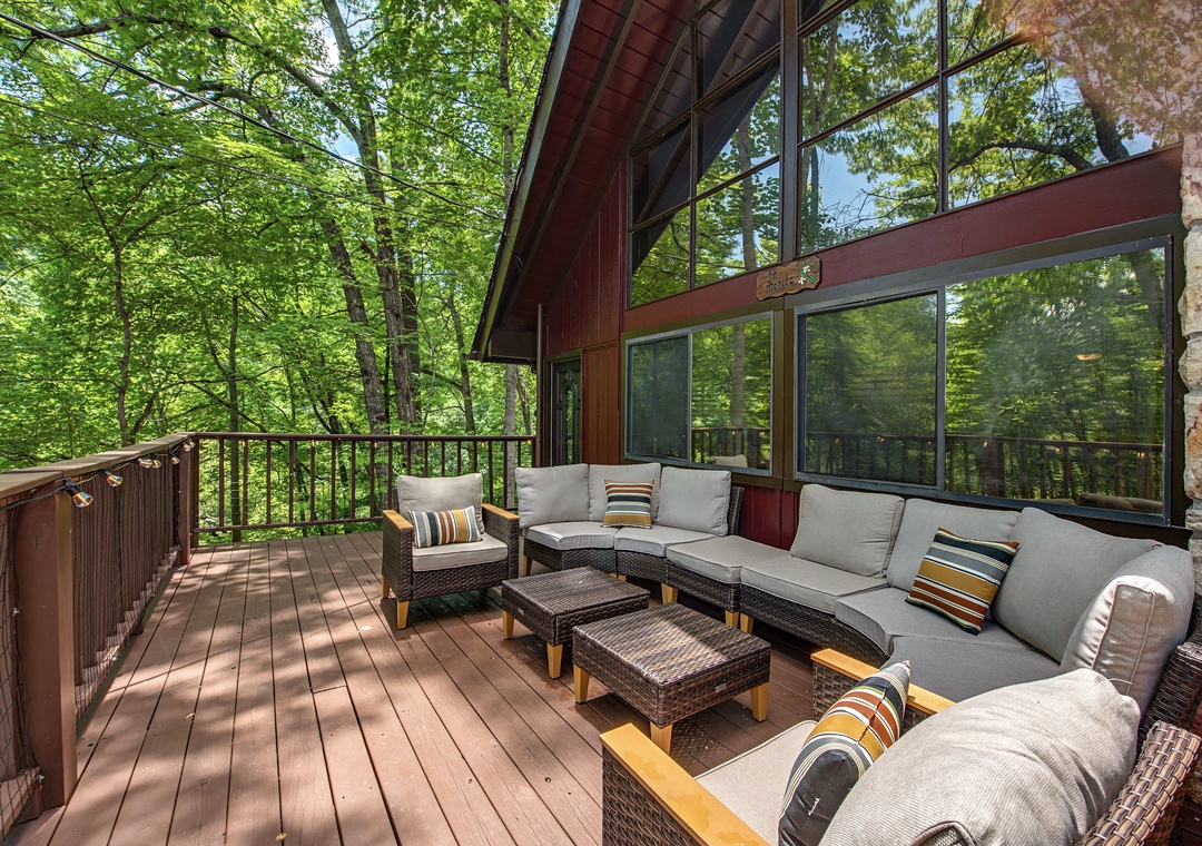 A sunny deck surrounded by lush greenery invites you to relax in comfortable seating while enjoying the peaceful forest views through large windows.