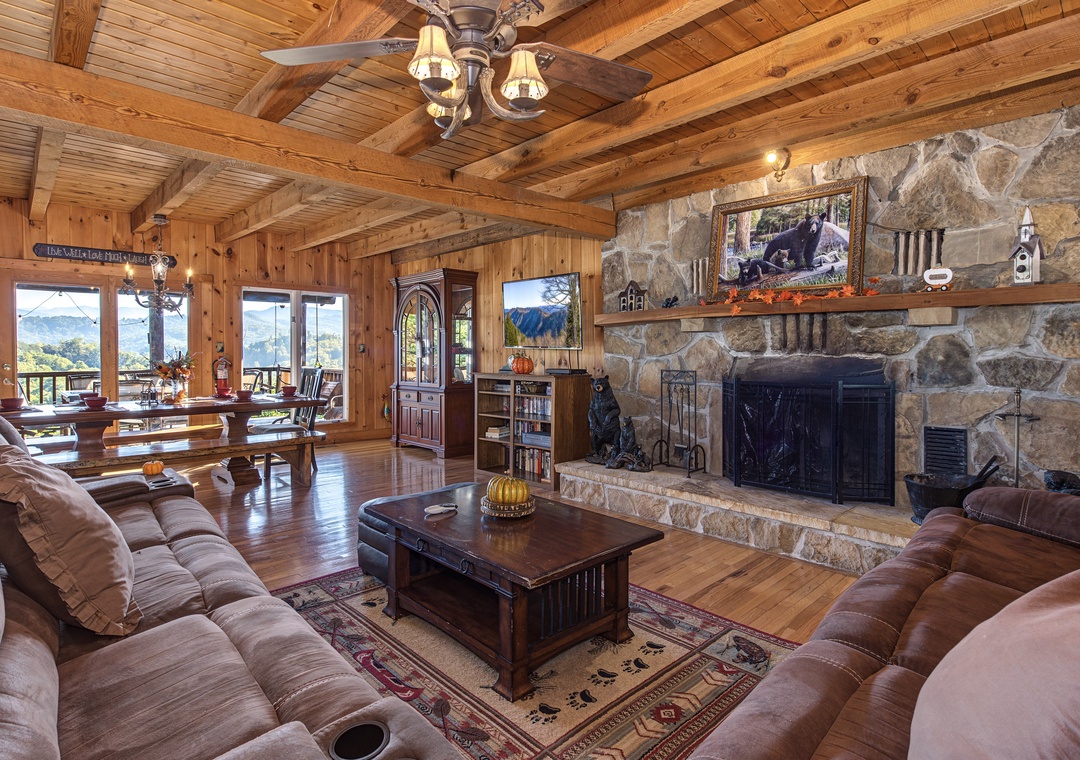 Settle into your cozy living room with soaring wood-beam ceilings, a grand stone fireplace, and sweeping mountain views through expansive windows—perfect for unwinding after a day of adventure.