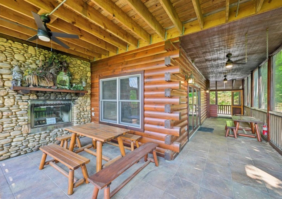 Gather around the stone fireplace on this covered porch, where rustic log benches and soaring timber ceilings create your perfect mountain retreat for cozy evenings.