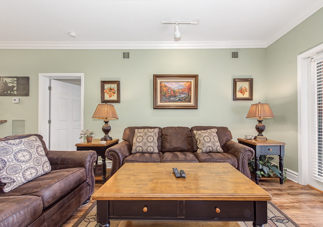 Sink into plush leather sofas in your cozy living room, where warm autumn artwork and soft lighting create the perfect atmosphere for relaxation.