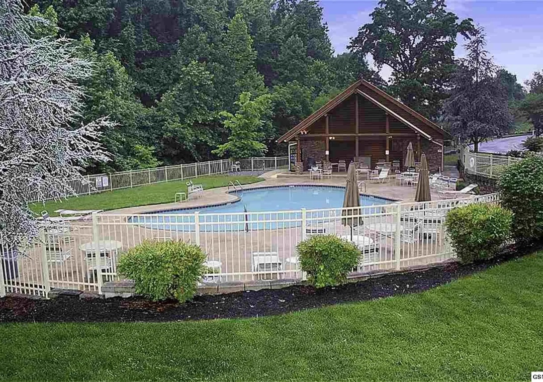 Private pool area with rustic cabin lodge surrounded by mature trees and landscaped grounds in a peaceful wooded setting.