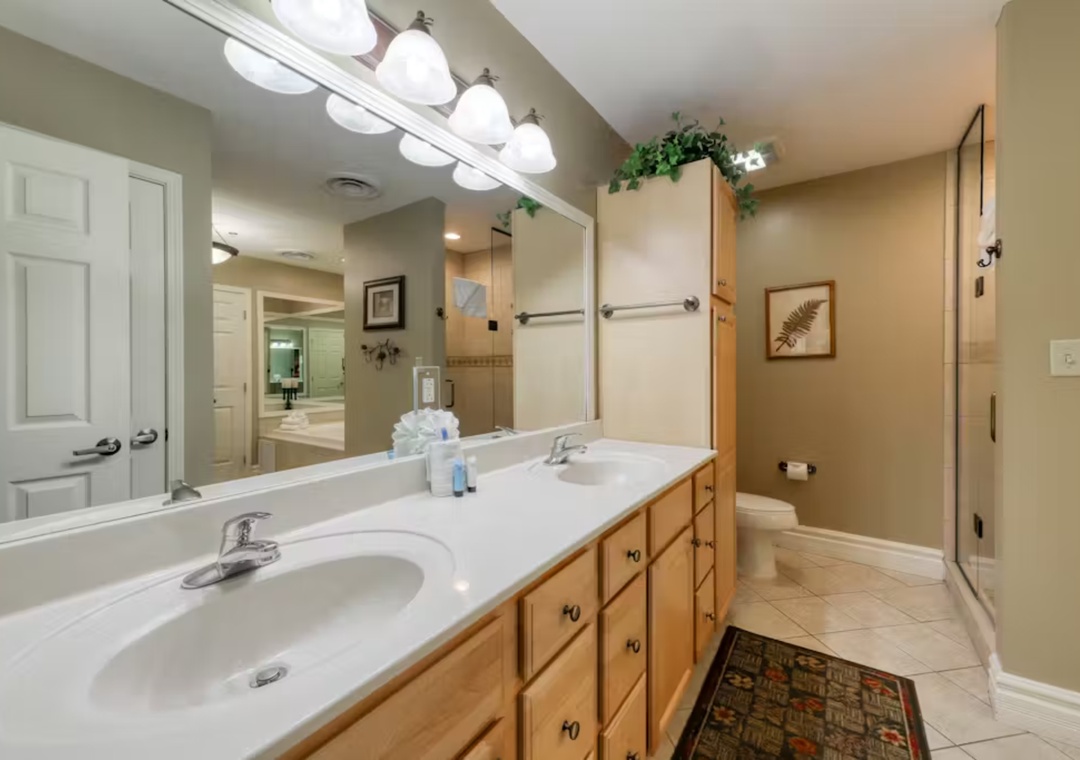 Refresh in your spacious master bathroom with dual vanities, warm wood cabinetry, and bright lighting for your morning routine.