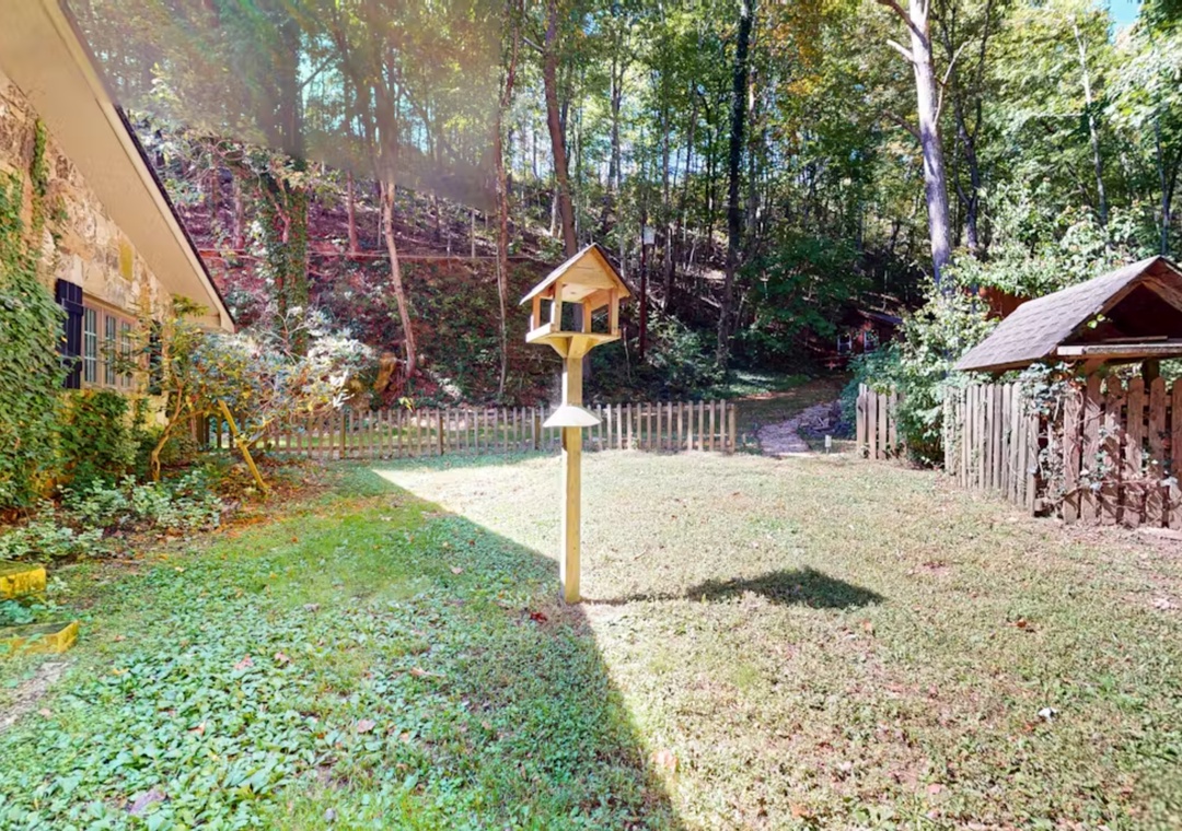 Property surrounded by lush forest with charming birdhouse and wooden shelter in peaceful outdoor space.