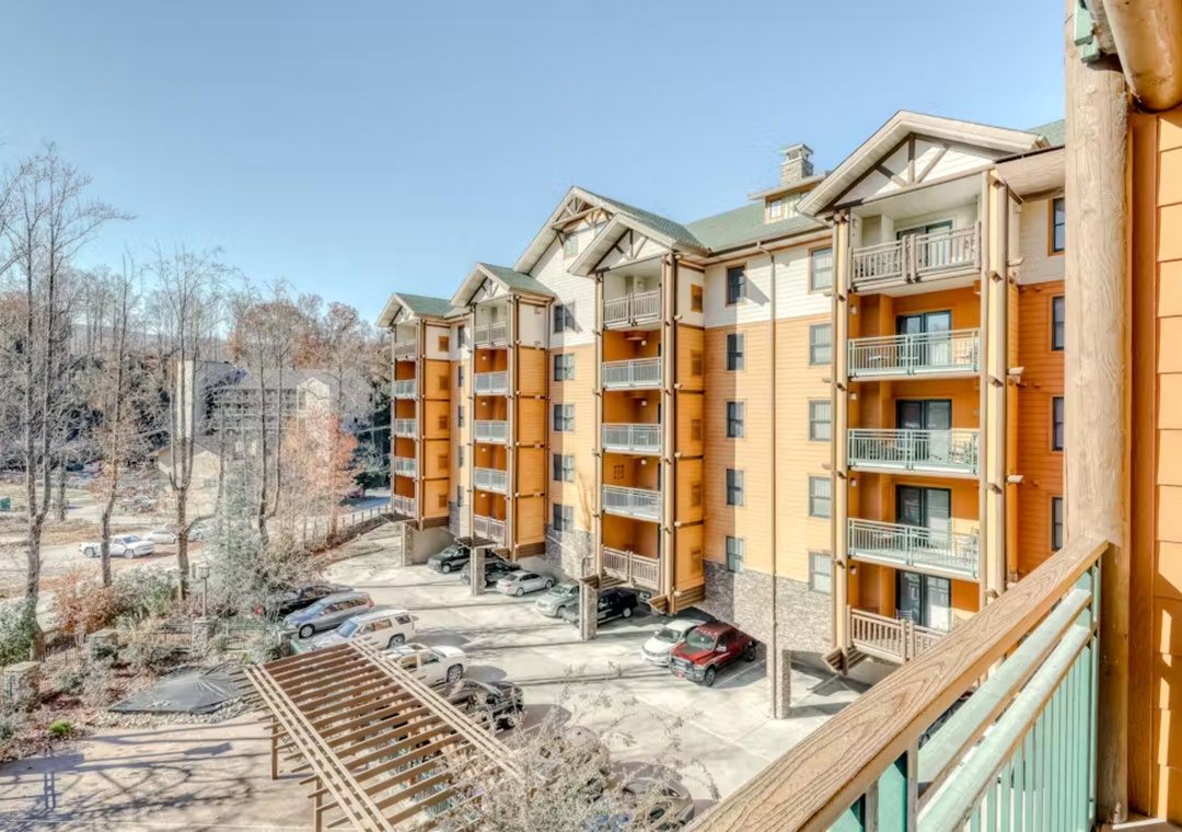 Mountain resort complex with multi-story buildings featuring private balconies and convenient parking areas set among wooded surroundings.