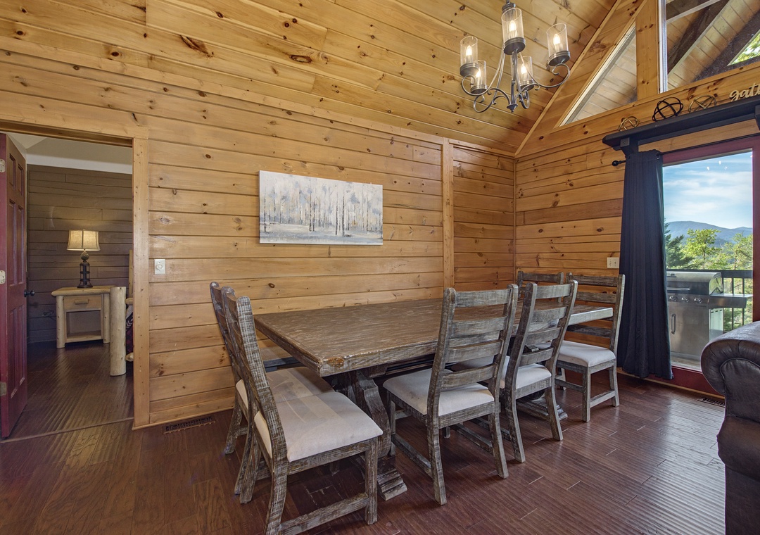 Gather around your rustic dining table where warm wood walls and charming chandelier create the perfect setting for memorable meals together.