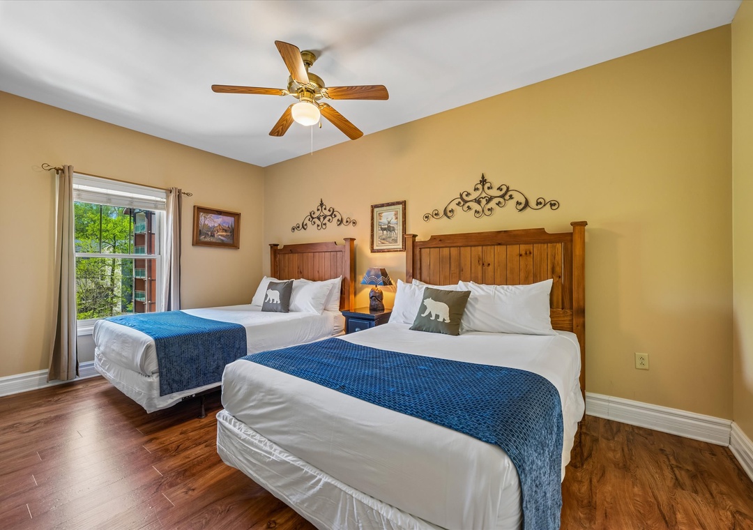 Rest comfortably in this charming twin bedroom featuring warm wood accents, cozy blue throws, and a peaceful garden view.