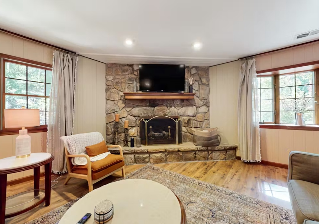 Cozy up by your private stone fireplace while enjoying natural light streaming through charming windows in this warm, inviting living space.