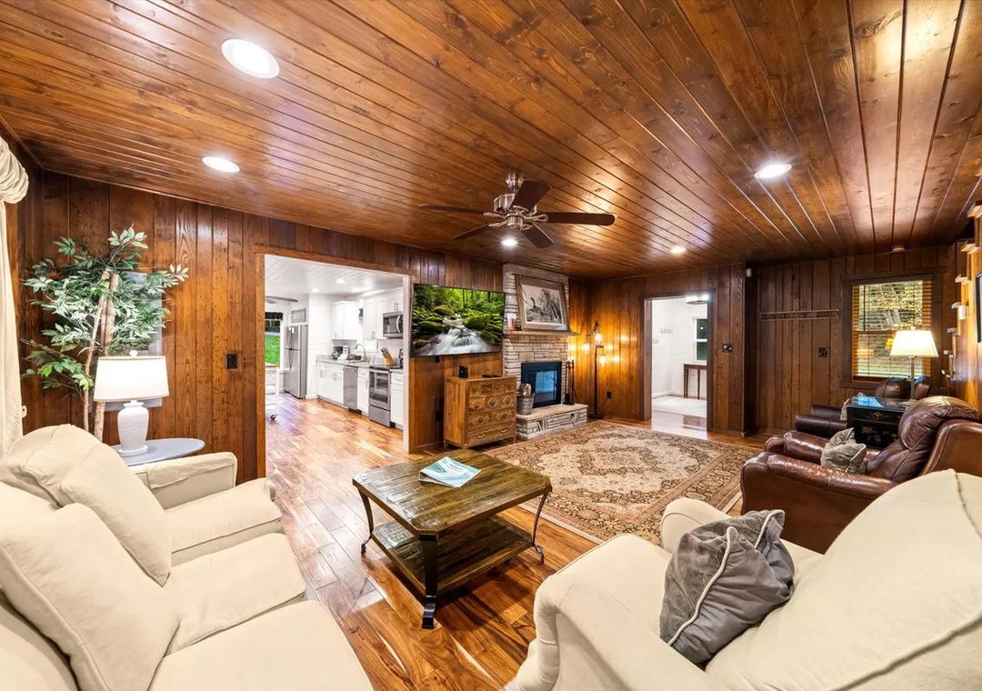 Step into the warmth of rich wood paneling and soaring vaulted ceilings that give this cozy living space its cabin-like charm. Sink into plush seating and enjoy your favorite shows while natural light filters through, creating a welcoming retreat.