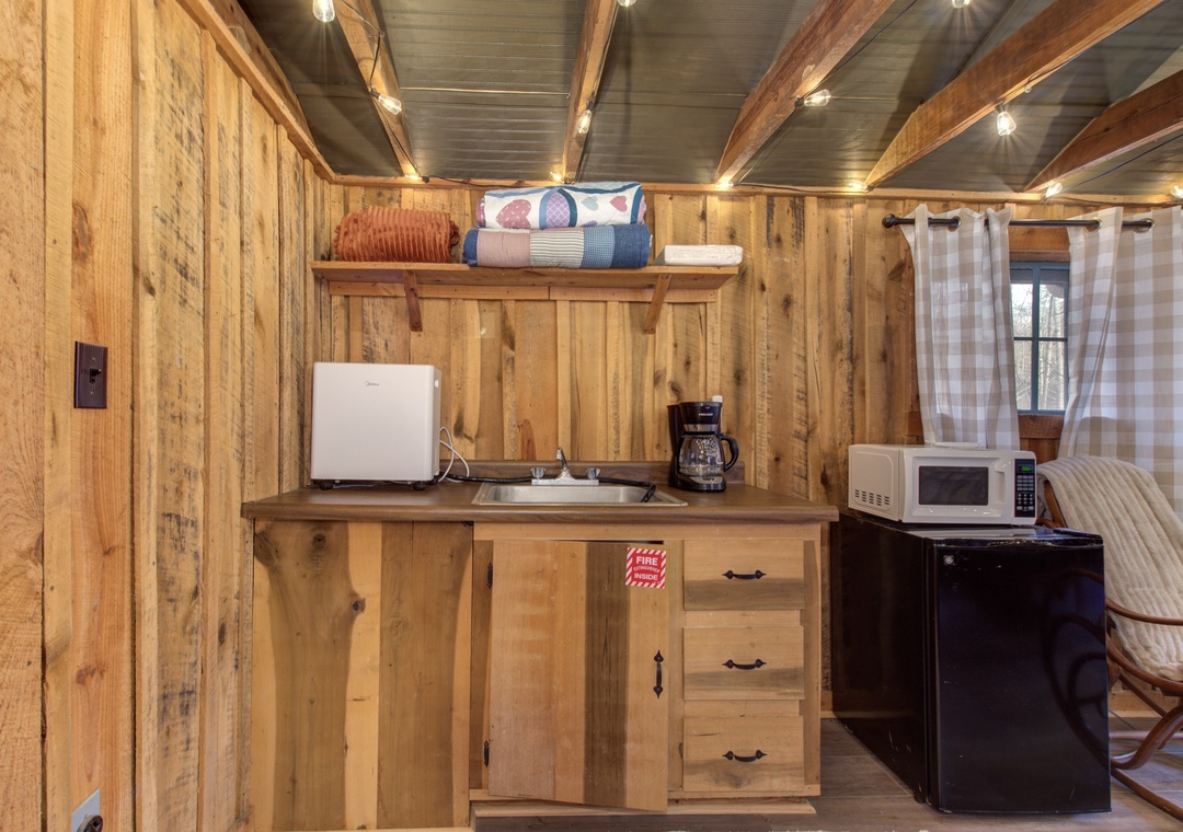Your cozy cabin kitchenette features rustic wood walls, warm lighting, and essential appliances for preparing simple meals during your retreat.