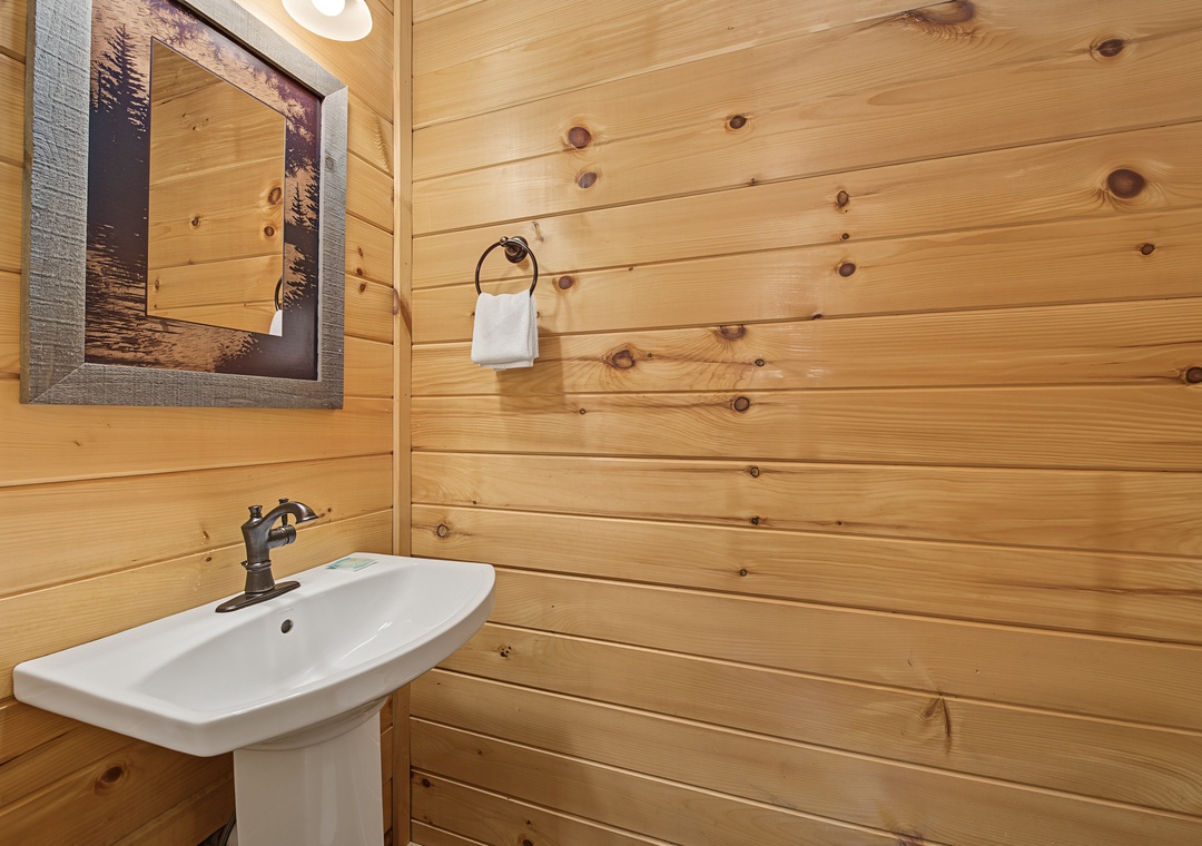 Rustic cabin charm meets modern convenience in this cozy bathroom, where warm wood paneling wraps around you and a crisp pedestal sink offers a refreshing place to start and end your day.