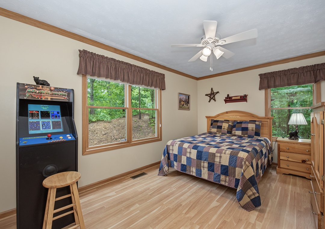 Your bedroom blends comfort and fun with a cozy quilted bed, classic arcade games, and peaceful green views to help you unwind after a day of adventure.