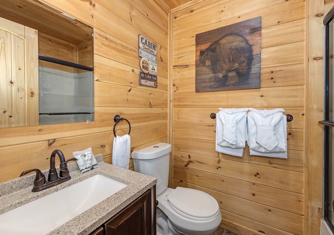 Rustic cabin charm meets modern comfort with warm wood paneling, fluffy white towels, and thoughtful touches that make your stay feel authentically cozy and completely convenient.