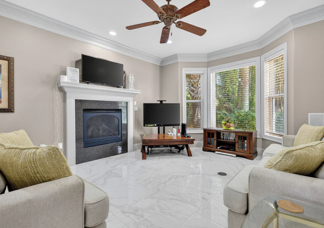 Unwind in your spacious living room with plush seating, a cozy fireplace, and entertainment setup. Bright windows fill the space with natural light as a ceiling fan keeps you comfortable year-round.