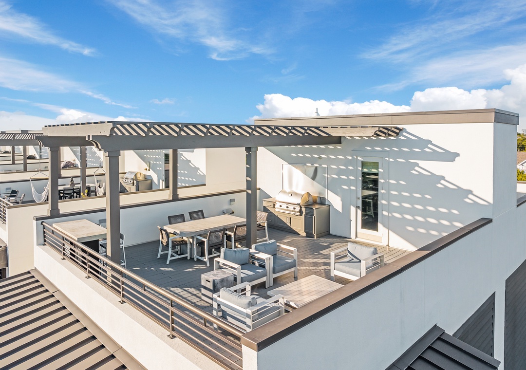 Stunning rooftop terrace with modern dining and lounge areas under stylish pergola, perfect for entertaining under bright blue skies.