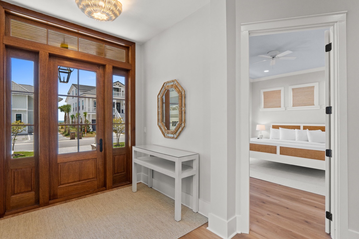 Bright entryway features elegant wood doors with transom windows and a glimpse into your coastal bedroom retreat. Natural light and thoughtful design welcome you home to relaxation.