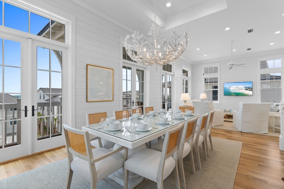 Step into an elegant dining space where coastal light pours through expansive windows, illuminating a beautifully set table beneath a stunning antler chandelier—perfect for gathering your group for memorable meals together.