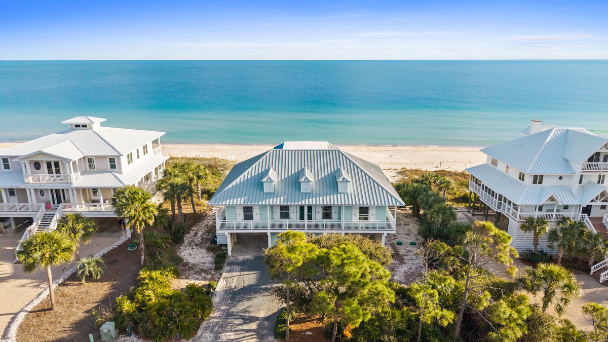 Beachfront vacation home with distinctive curved metal roofing sits steps from pristine turquoise waters and white sand beach.