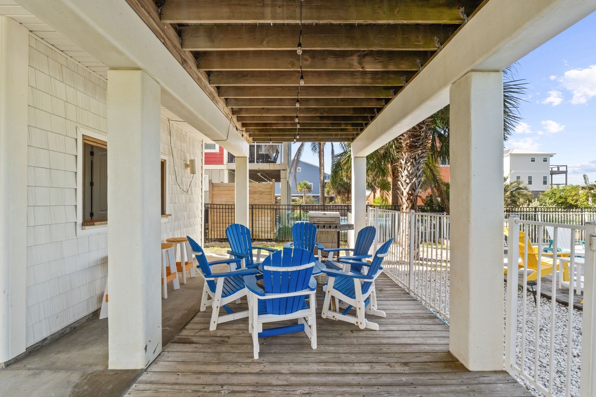 Gather with friends on your covered deck, where bright blue Adirondack chairs invite easy conversation and the warm coastal breeze flows freely through this welcoming outdoor retreat.