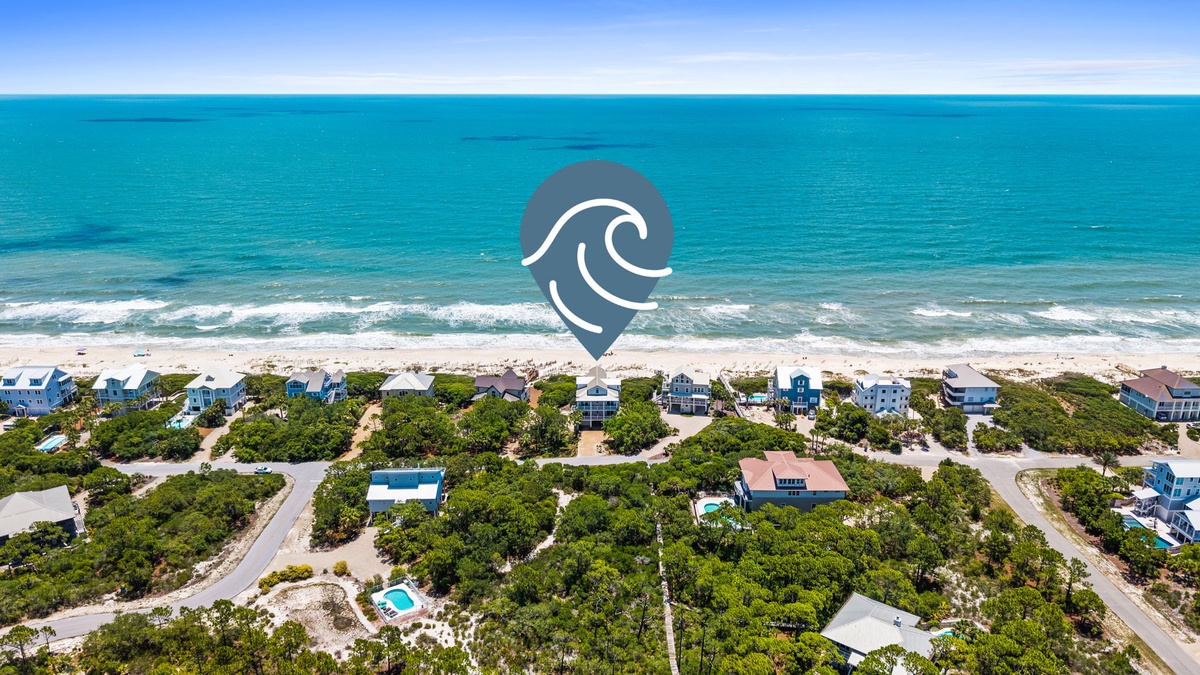 Aerial view of a coastal vacation rental community nestled among lush greenery, with pristine white sand beaches and turquoise ocean waters stretching to the horizon.