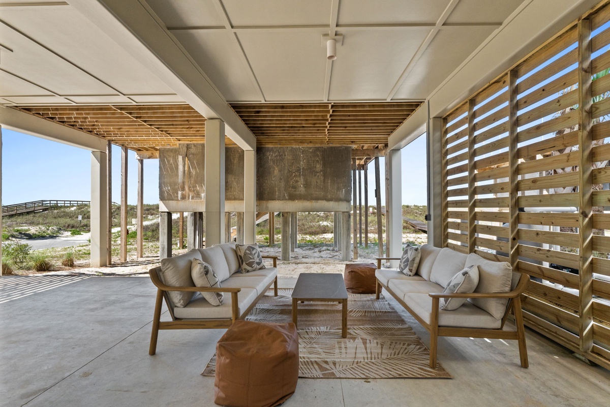 This covered outdoor lounge opens to coastal dunes and sea breezes, offering you a serene space to unwind with plush seating and natural textures just steps from the beach.