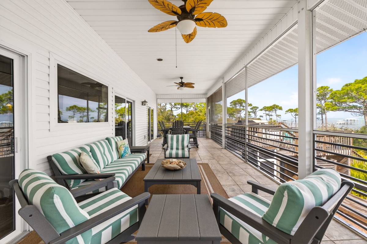 Relax on your private covered porch with coastal views, tropical ceiling fans, and comfortable striped seating perfect for morning coffee or sunset cocktails.
