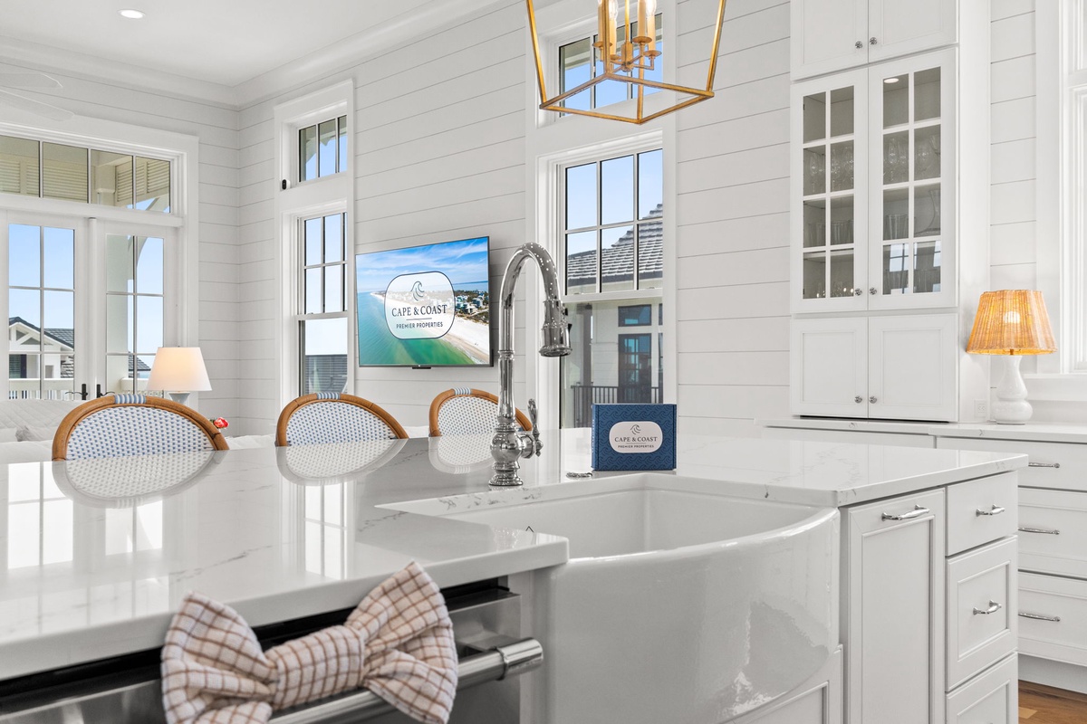 Your coastal-style kitchen features a spacious farmhouse sink, bright white cabinetry, and charming shiplap walls bathed in natural light—perfect for preparing meals with family and friends.